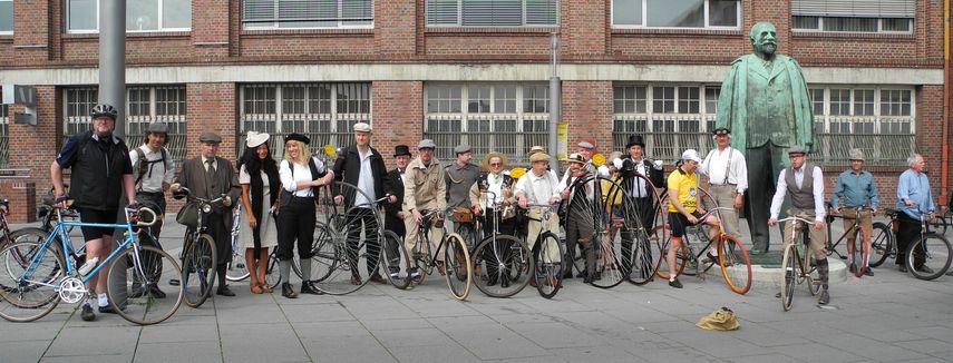 Datei: DSCN1168.jpg; Breite: 855px; Höhe: 326px - Die Teilnehmer der geführten Tour vor dem Adam Opel Denkmal am alten Opel Hauptportal, Bahnhofsplatz